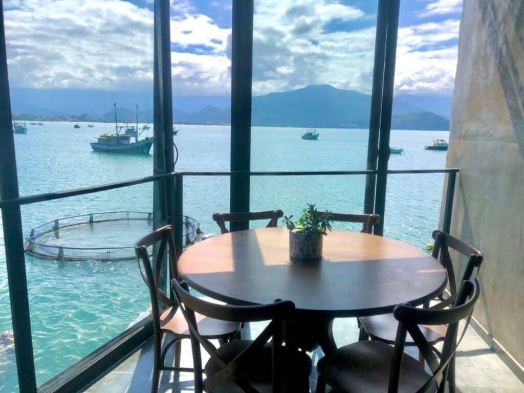 Sala do 1819 Marine Hotel com uma mesa redonda de seis lugares cercada por paredes de vidro com vista para o mar