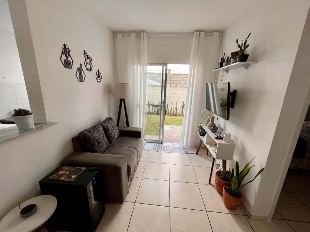Sala de apartamento para aluguel de temporada com sofá, TV, luminária, porta para quintal e vasos decorativos. Imagem para ilustrar o post hotéis em Campina Grande.