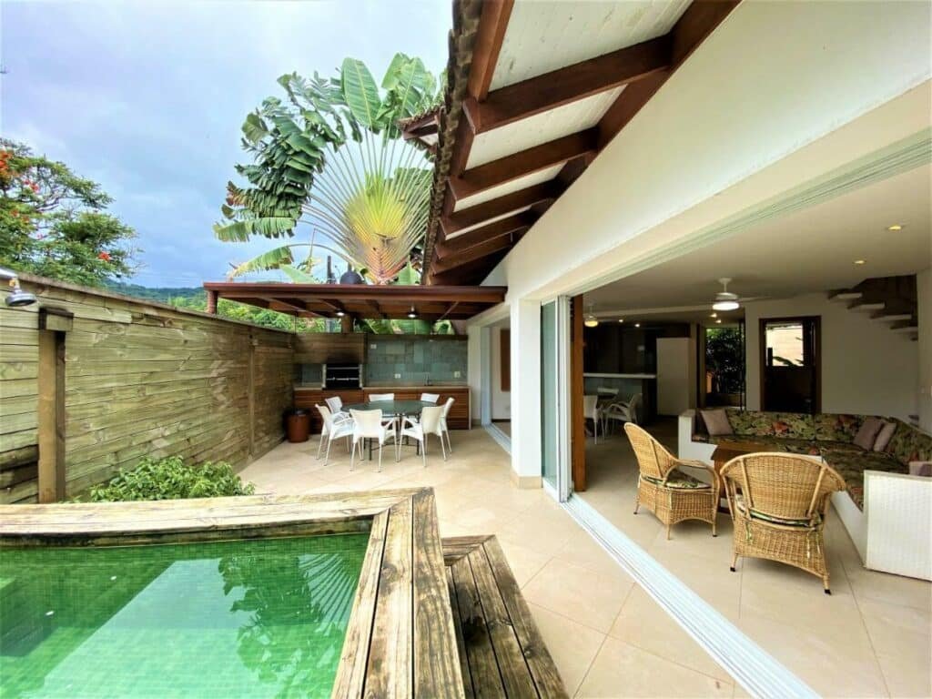 Área de lazer da Casa na Praia Maravilhosa com piscina no canto esquerdo da imagem a frente, do lado direito sofá com poltronas.