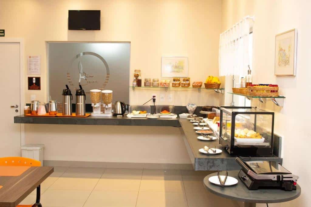 Bancada de café da manhã com garrafas de café, pratos com pães, bolos e frutas.
