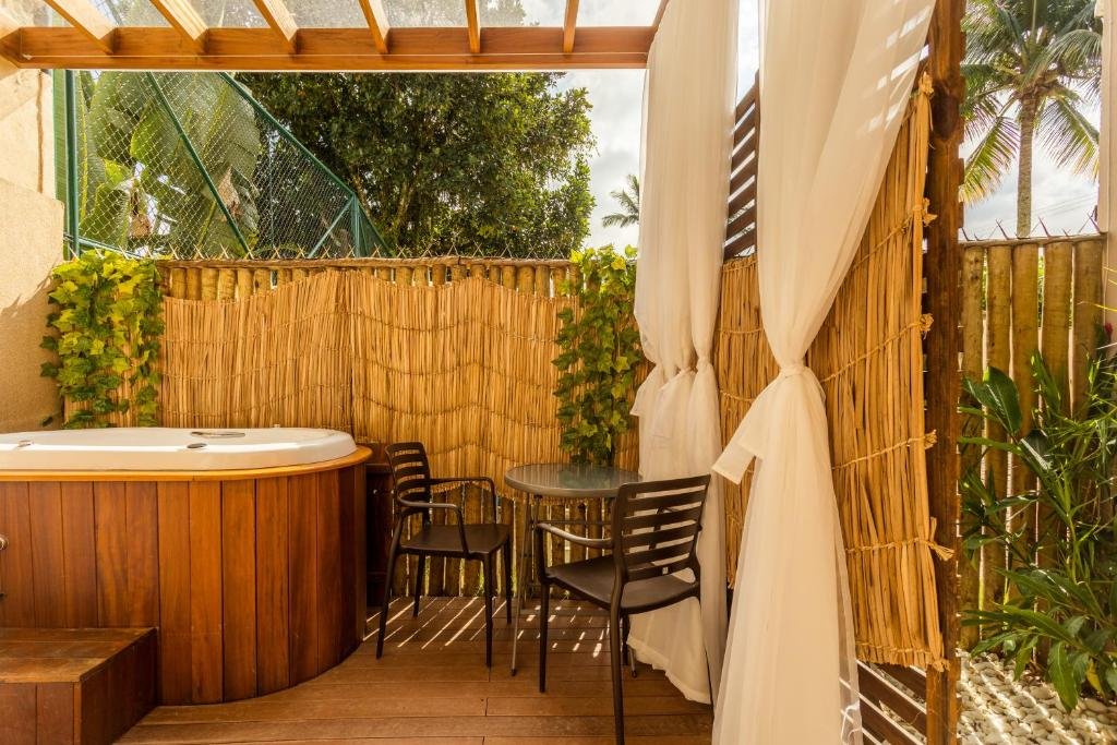Área de lazer da Casa d’Aroeira Condomínio Residencial Luxo com uma mesa redonda a frente com duas cadeiras e do lado esquerdo da mesa uma banheira de hidromassagem.