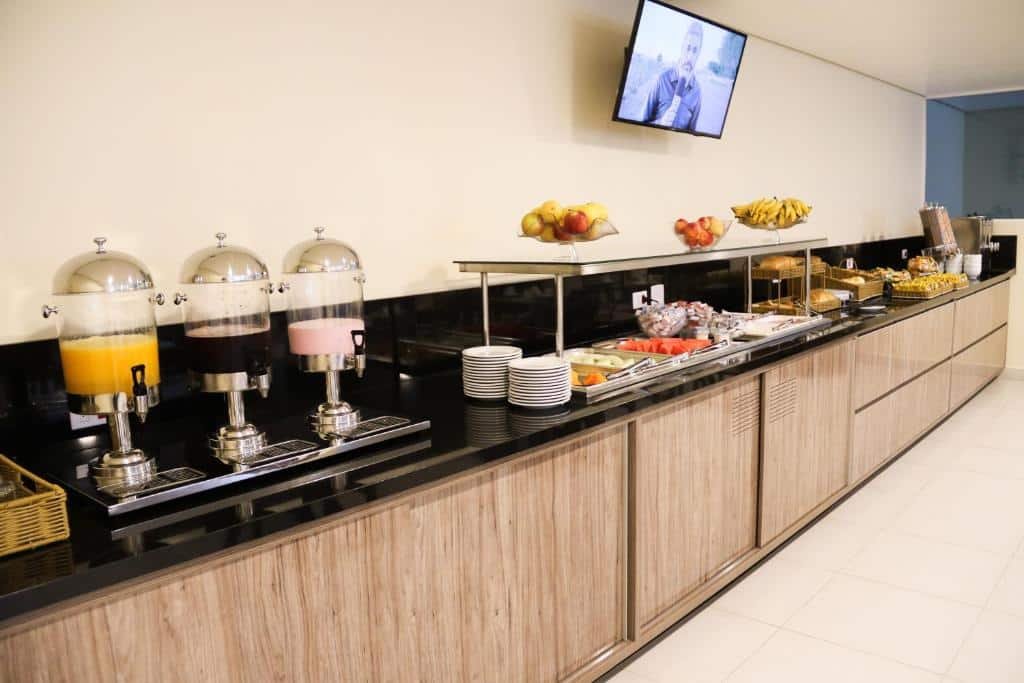 Café da manhã no Hotel Vale das Artes. Uma bancada com o café da manhã. Com sucos, pratos, frutas, frios, pães, bolachas e bolos. Foto para ilustrar post sobre Pousadas em Embu das Artes.