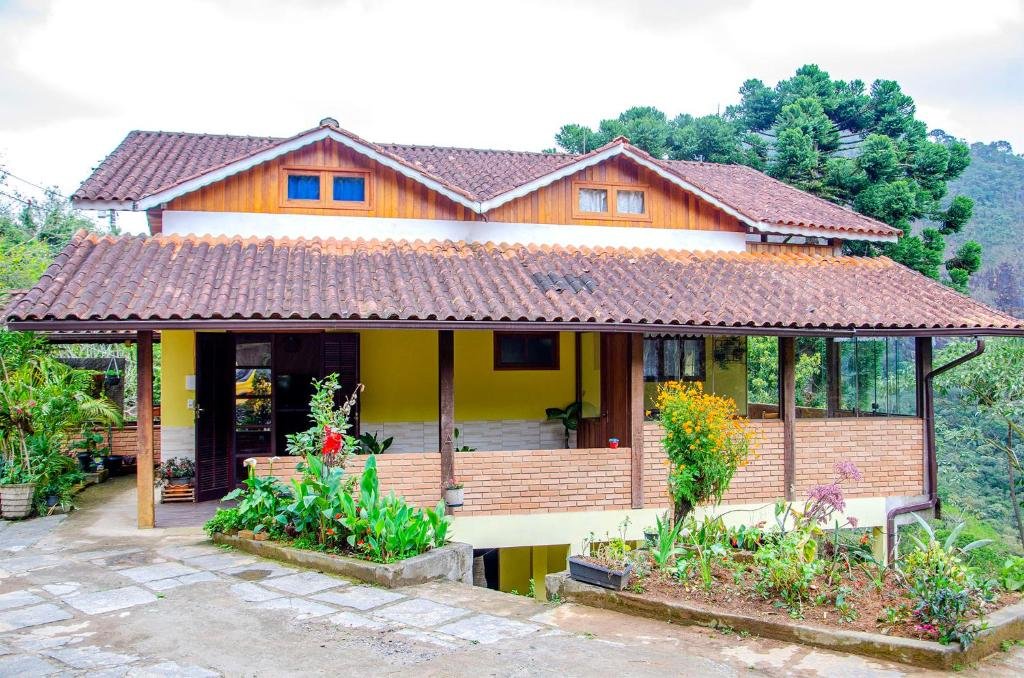 Casa amarela grande com detalhes em madeiras e tijolos com pequenas plantas em volta durante o dia, ilustrando post pousadas em Visconde de Mauá.