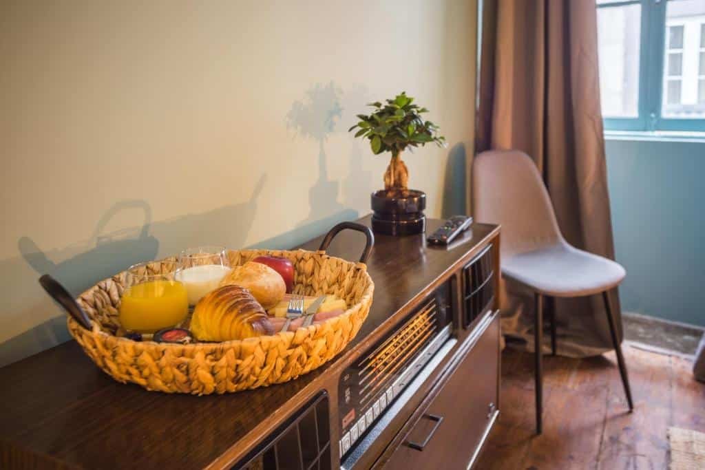 Cesta de café da manhã do Laurear Guest House com pães, frios, suco e leite em cima de uma cômoda no quarto.