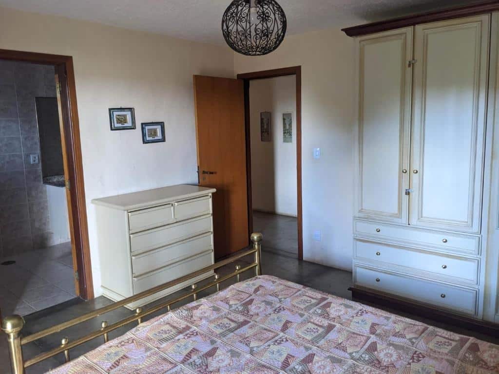 Foto do quarto em Chácara Santa Terezinha. A cama está no meio, vemos ela como quem está sentado. O guarda-roupa está ao lado direito, e também a porta do quarto. De frente há uma cômoda e porta para o banheiro, mais à esquerda. 
Ilustra o post sobre airbnb em Serra Negra.