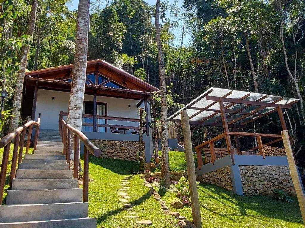 Uma das hospedagens do chalé au clair de lune terê com uma escada para o acesso ao chalé, gramado e árvores ao fundo, ilustrando post pousadas em Teresópolis.