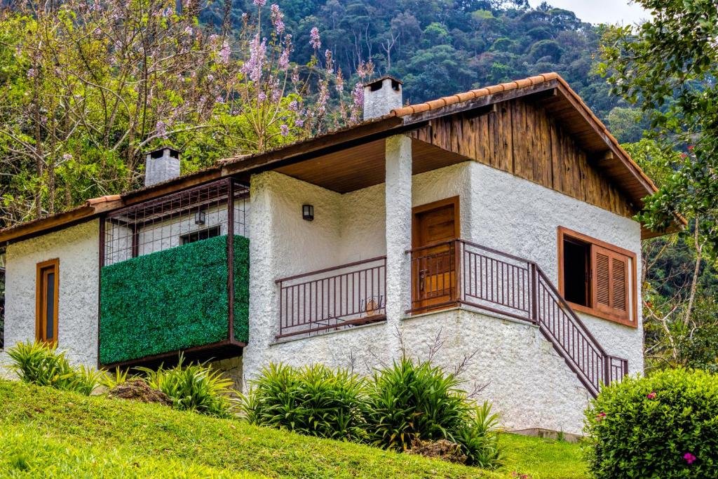Grande chalé branco com detalhes em madeira em cima de um gramado e com árvores em volta durante o dia, ilustrando post pousadas em Visconde de Mauá.