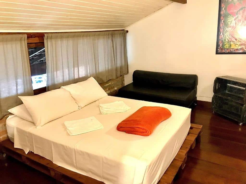 Quarto de um dos Chalés Água Grande. O teto é baixo e uma cama de casal está em cima de um apoio de madeira. Um sofá está ao lado da cama, assim como duas prateleiras.