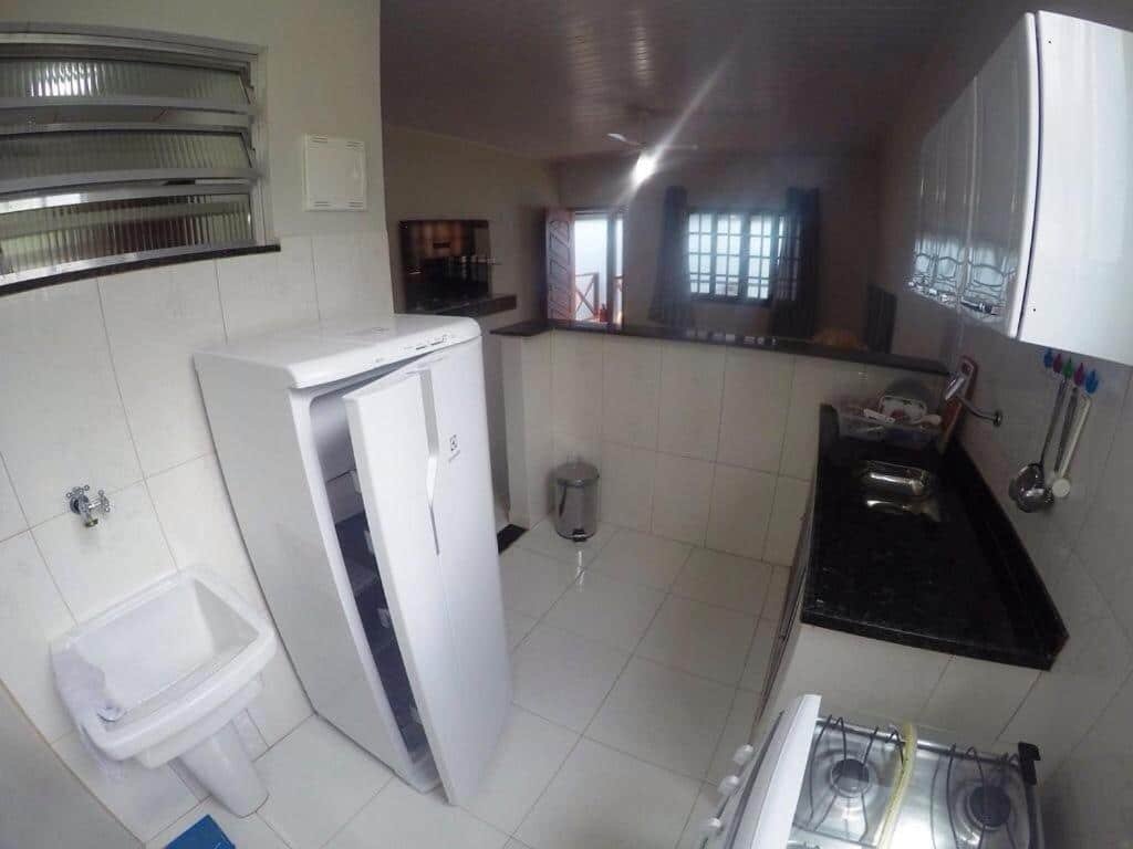 Cozinha do airbnb Suítes do Cid. No lado direito há uma pia com um armário em cima e o fogão, no lado esquerdo há um tanque e uma geladeira e atrás há um balcão que divide a cozinha do resto do airbnb.