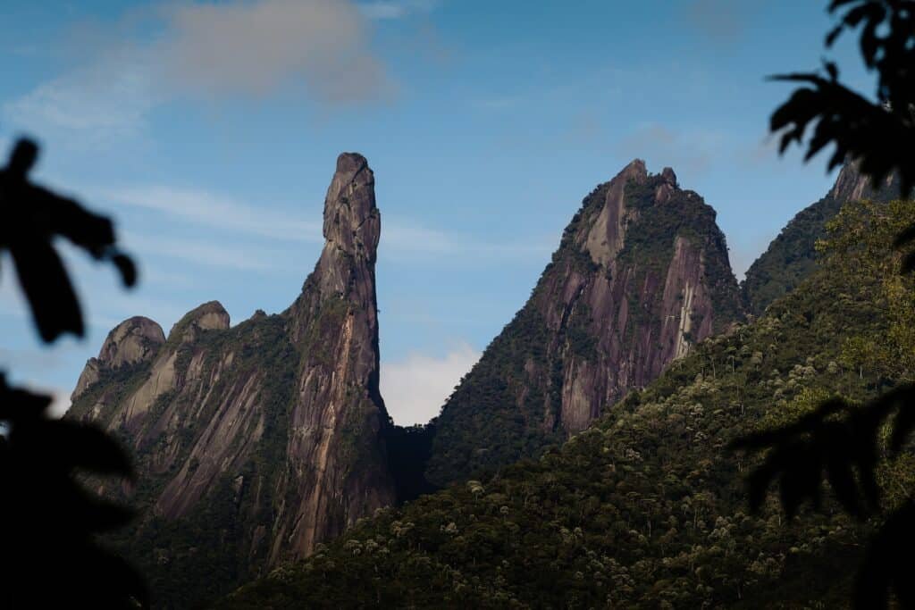 Pico chamado "Dedo de Deus" com bastante árvores verdes em volta durante o dia, ilustrando post pousadas em Teresópolis.