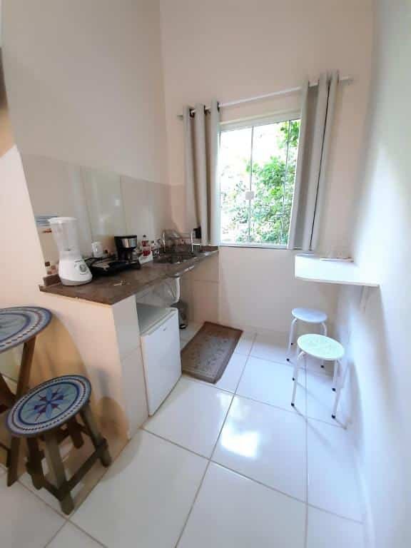 Cozinha do airbnb Flats Jordão. No lado direito há uma mesa presa na parede com dois banquinhos em baixo e no lado esquerdo está o balcão da cozinha com um frigobar em baixo.