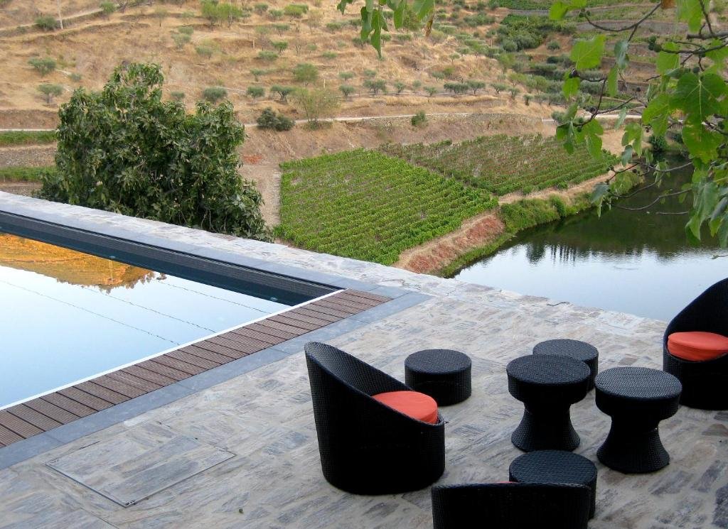 Área da piscina do Quinta do Tedo durante o dia, com cadeiras e puffs do lado direito da imagem, do lado esquerdo da imagem a piscina com vista para o rio e a vinha.