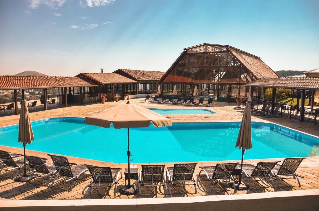 Piscinas do Guararema Parque Hotel, sendo uma grande e outra menor, com espreguiçadeiras em volta e prédios com paredes de vidro da pousada ao fundo. A imagem é num dia ensolarado e serve para ilustrar o post de pousadas em Guararema