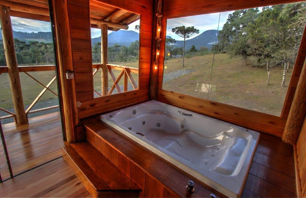 Uma banheira de hidromassagem, ao redor vidro com vista para a área verde da Hospedaria Refugio do Invernador.