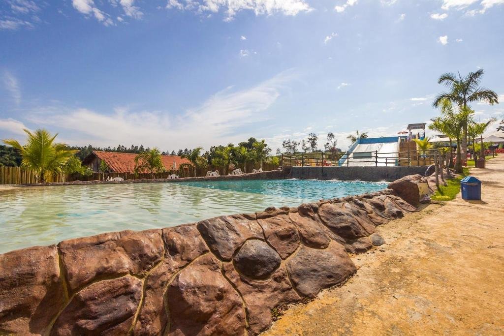 Piscina com bordas de pedra do Hotel Fazenda Pintado na Brasa, com algumas árvores em volta e um escorregador aquático ao fundo. Imagem para ilustrar o post de pousadas em Guararema