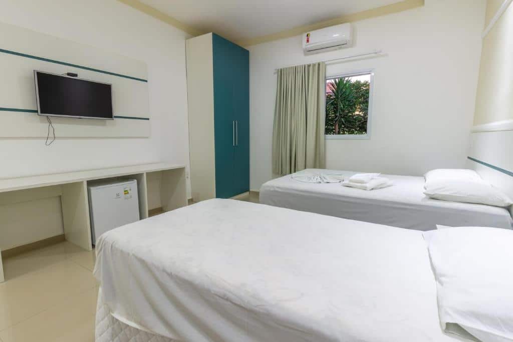 Quarto do Hotel Fazenda Pintado na Brasa, de 18 m², com duas camas de solteiro, frigobar, TV suspensa, armário de duas portas e ar-condicionado. Há uma janela com vista para árvores verdes