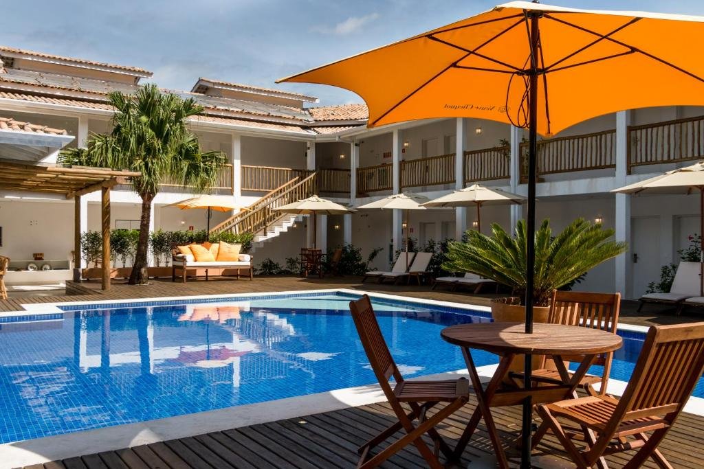 Piscina do Hotel Maui Maresias com as sacadas da propriedade viradas em direção da piscina, ao redor há um deck de madeira com cadeiras, mesas e guarda-sóis
