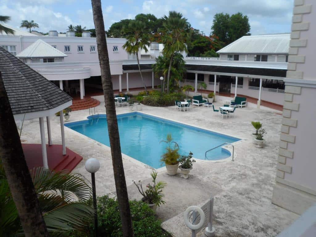 Área externa do Hotel PomMarine. Uma piscina ao ar livre no centro, o redor cadeiras e mesas. Imagem ilustrando post Hotéis em Barbados.