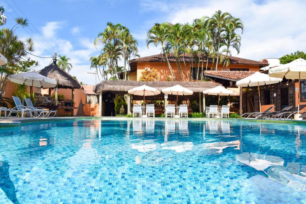 Piscina da Hotel Pousada dos Condes com cadeiras e guarda-sóis brancos ao redor e alguma palmeiras perto da propriedade