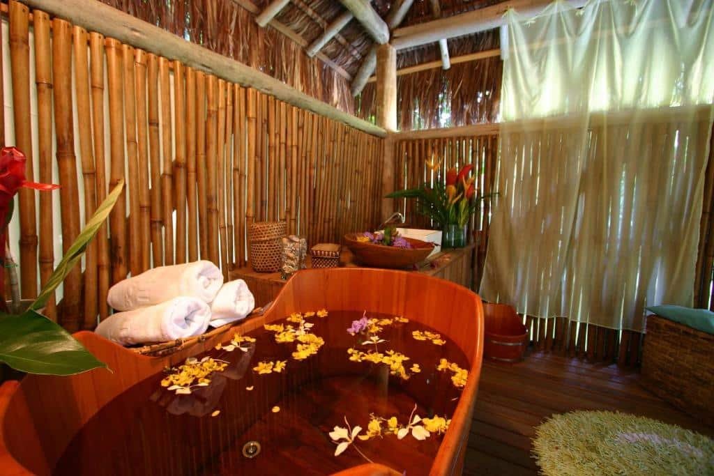Banheira no Itamambuca Eco Resort com muitas flores dentro, um deck de madeira ao redor com plantas e toalhas ao redor