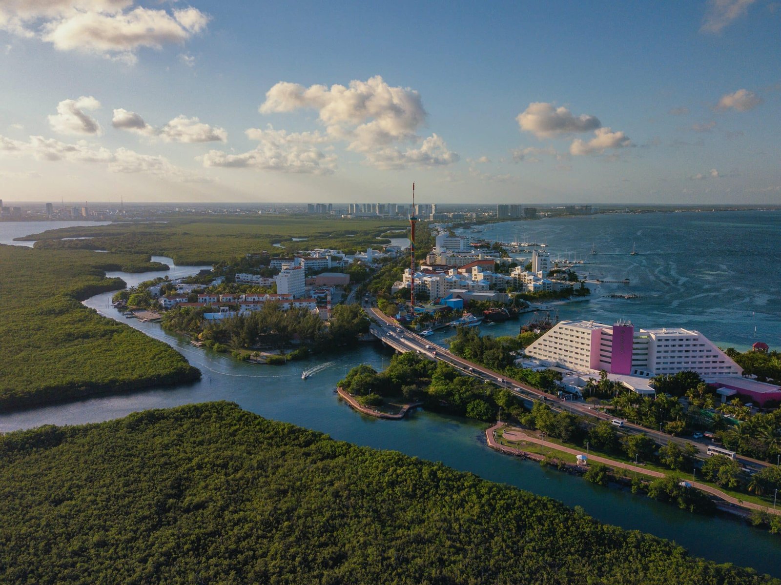 vista aerea da Kukulcan Boulevard, Zona Hotelera em Cancun com um céu claro e algumas nuvens ao fundo, mostrando parte de terra verde e braços do mar entrando no continente