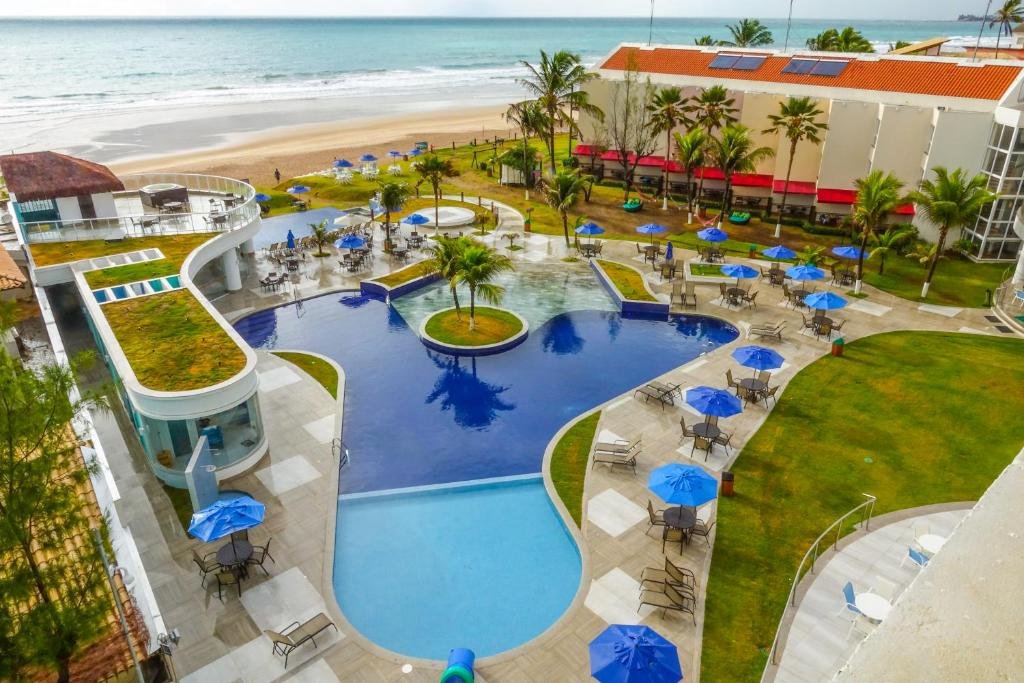 Piscina do Marupiara Resort de frente para a praia, entre os espaços da piscina há algumas árvores e pequenos gramados, além de espreguiçadeiras e guarda-sóis