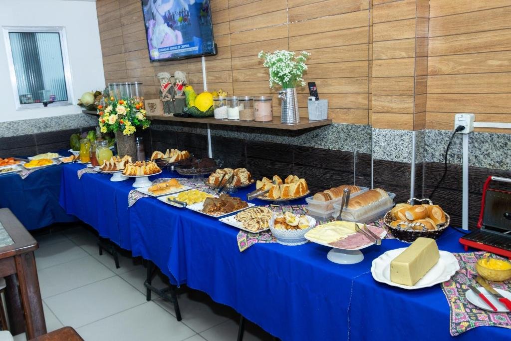Mesa com toalha azul e café da manhã de hotel, pratos com bolos, doces, salgados, pães e frios.