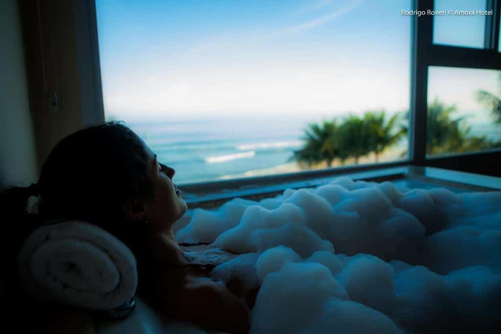 Mulher deitada na banheira no Amora Hotel no final do dia com vista para o mar.