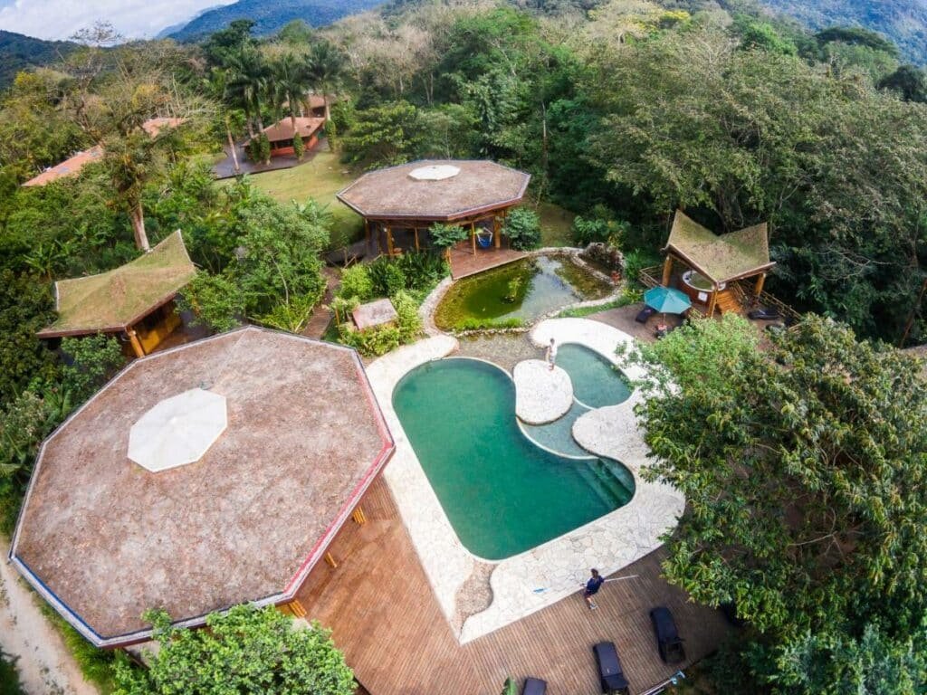 Piscinas do Banana Bamboo Ecolodge vistas de cima, há duas piscinas interligadas e, ao lado delas, uma lago com pedras, a propriedade é cercado por árvores e montanhas