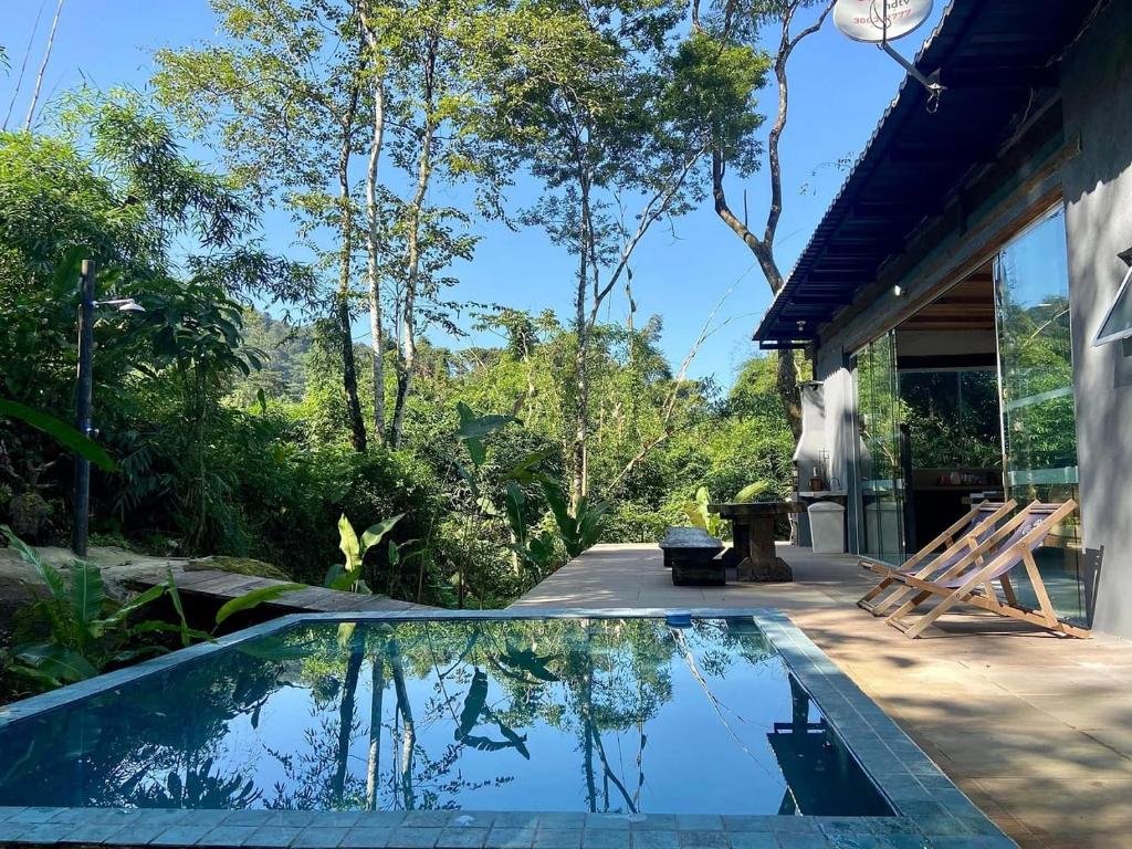 Piscina da Casa de Vidro com vista para o mar durante o dia com piscina a frente do lado esquerdo ao fundo do lado direito a propriedade.