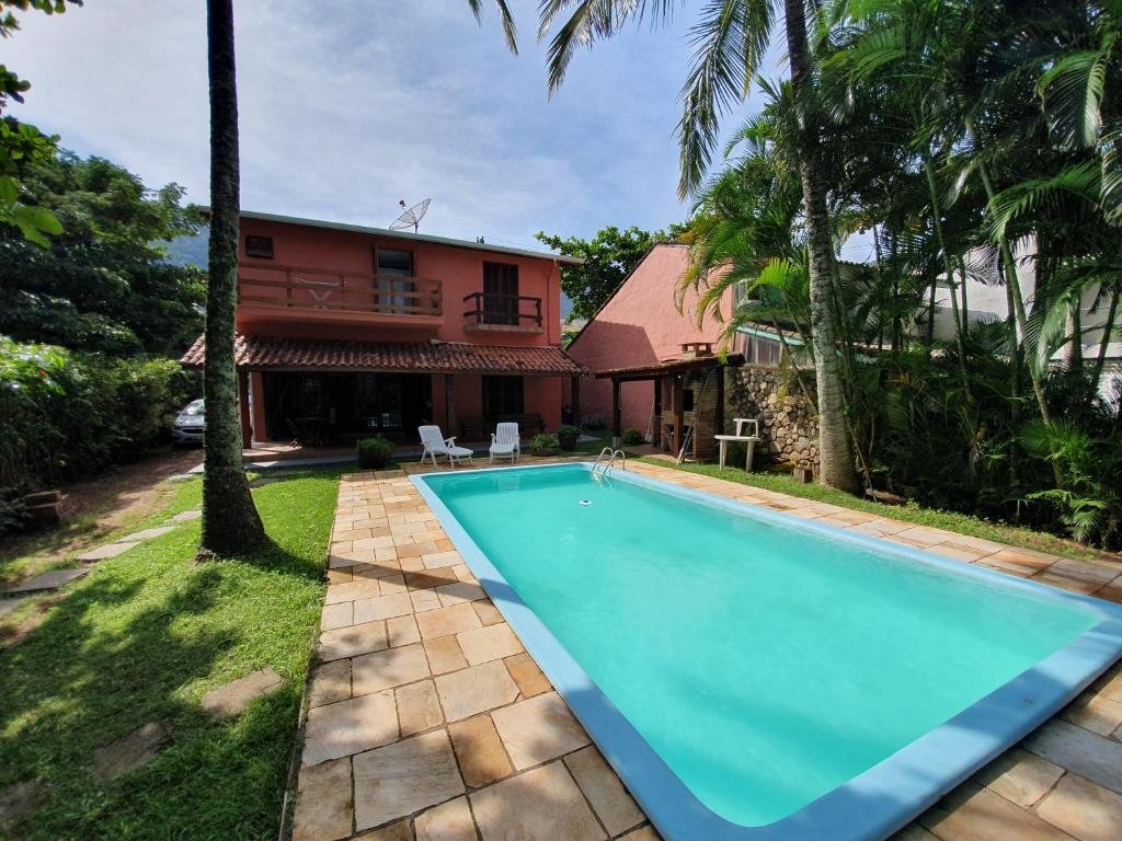 Piscina em Casa pé na areia em Toque Toque, uma ampla piscina aos fundos da casa, muitas árvores ao redor, algumas cadeiras, uma pequena churrasqueira e um pequeno gramado