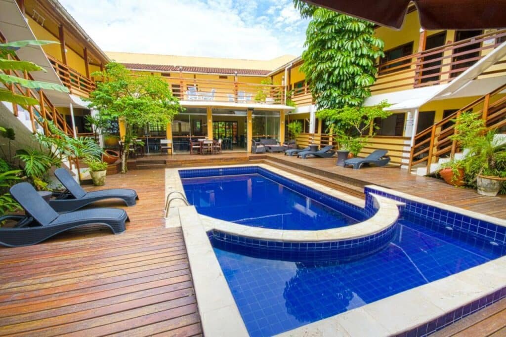 Piscina do Flat Vila Morena a pousada da sua família durante o dia. Com piscina no meio e no lado direito e esquerdo cadeiras e ao fundo a estadia.