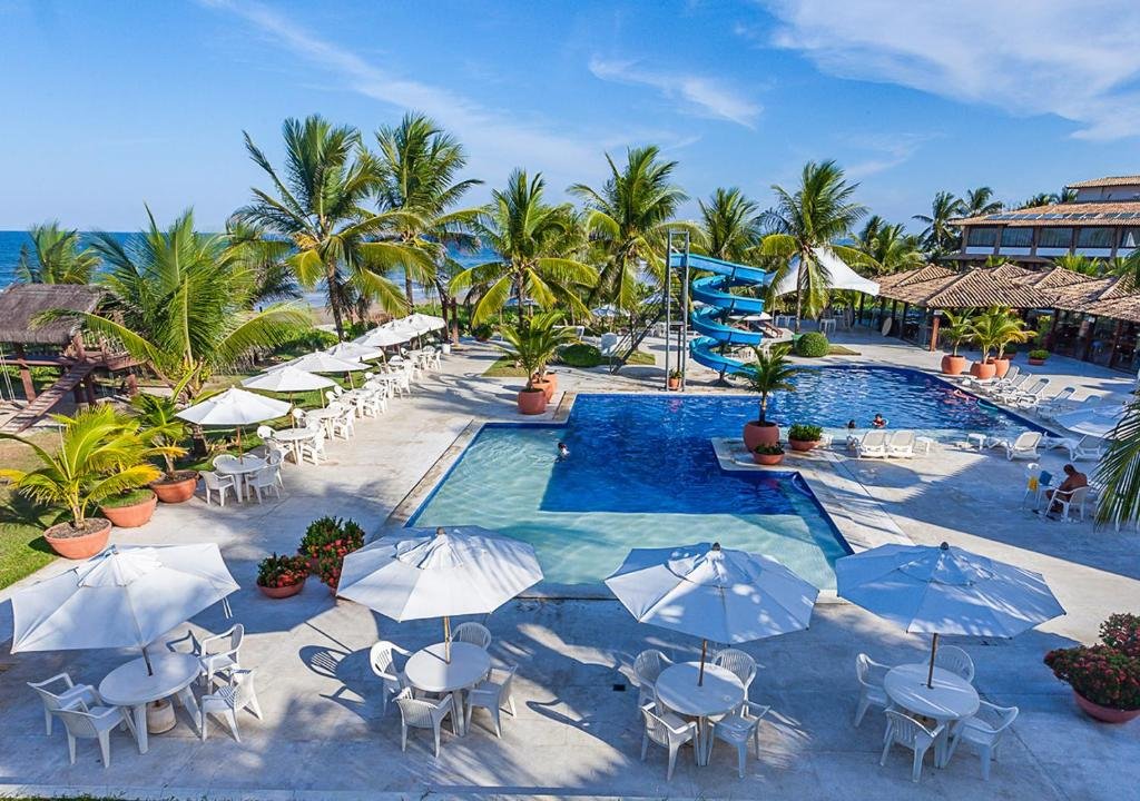 Piscina e área de lazer com mesas e cadeiras no Hotel Praia do Sol em Ilhéus.