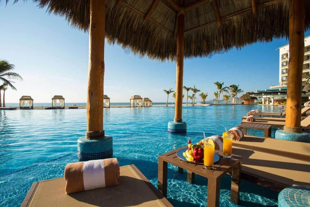 Vista da piscina do Hyatt Ziva Los Cabos – All Inclusive com cadeiras dentro da água e com vista para o mar e céu azul. Representa hotéis em Los Cabos.