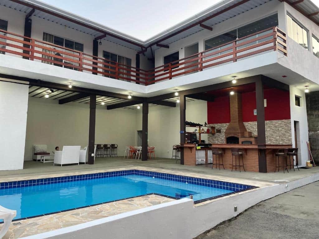 Uma rampa, e uma piscina do lado na Pousada Uchimura. Atrás uma churrasqueira com um balcão e uma área de lazer com sofás.
