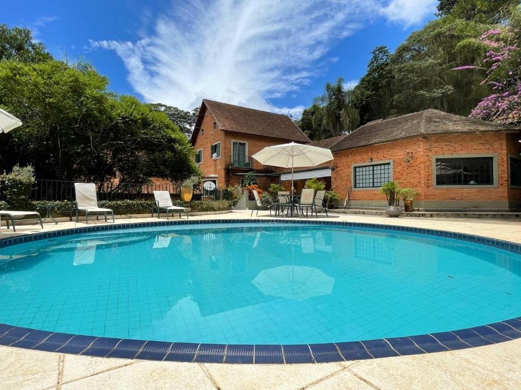 Pousada Villa Serena Bed & Breakfast. Uma piscina redonda, cadeiras ao redor e a pousada no fundo. Foto para ilustrar post sobre Pousadas em Embu das Artes.