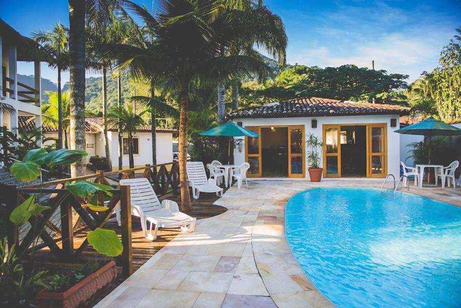 Área de lazer da Pousada Casarão com piscina do lado direito da imagem, do lado esquerdo cadeiras e ao fundo a estadia. Representa airbnb na Barra do Sahy.