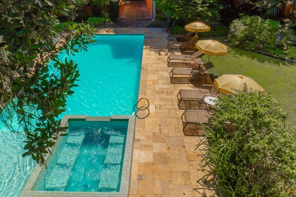 Piscina ampla na Pousada Jamboo com um gramado ao redor, espreguiçadeiras e alguns guarda-sóis
