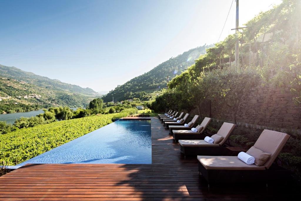 Área da piscina do Quinta de S.Bernardo – Winery & Farmhouse durante o dia, com cadeiras do lado direito e piscina do lado esquerdo com vista para o rio Douro.