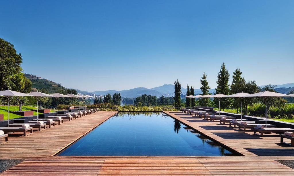 Piscina do Six Senses Douro Valley, durante o dia com piscina ao centro da imagem e no lado direito e esquerda dela cadeiras com guarda-sóis.