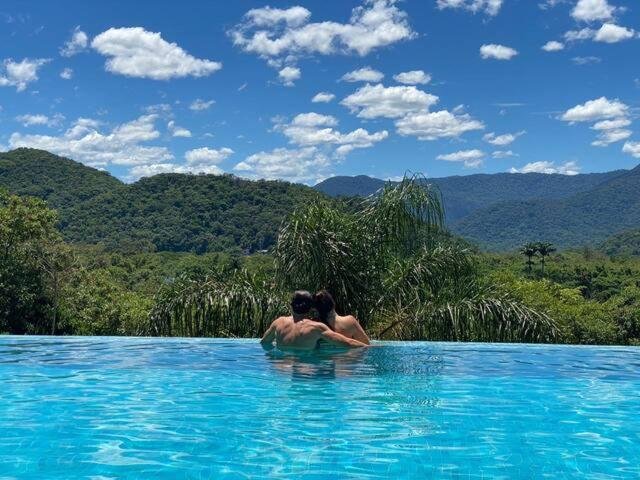 Um casal dentro da piscina do Vista Mágica na Praia de Camburizinho durante o dia com piscina a frente e ao fundo o casal.