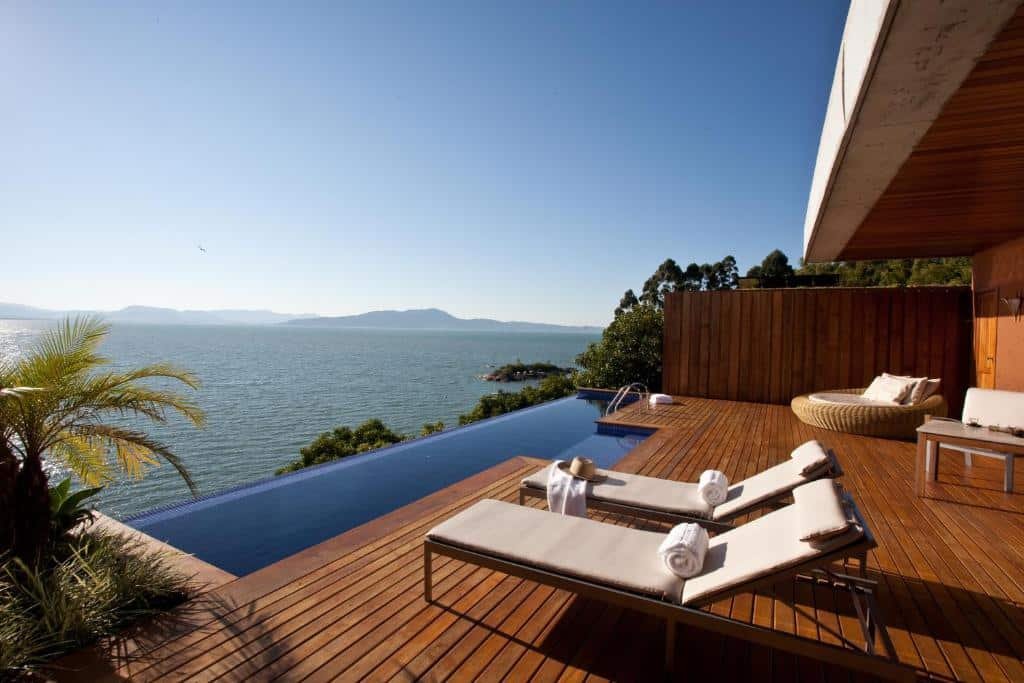 Varanda do Ponta dos Ganchos Exclusive Resort. Do lado direito cadeiras de tomar sol, do lado esquerdo uma piscina de borda infinita com vista para o mar.