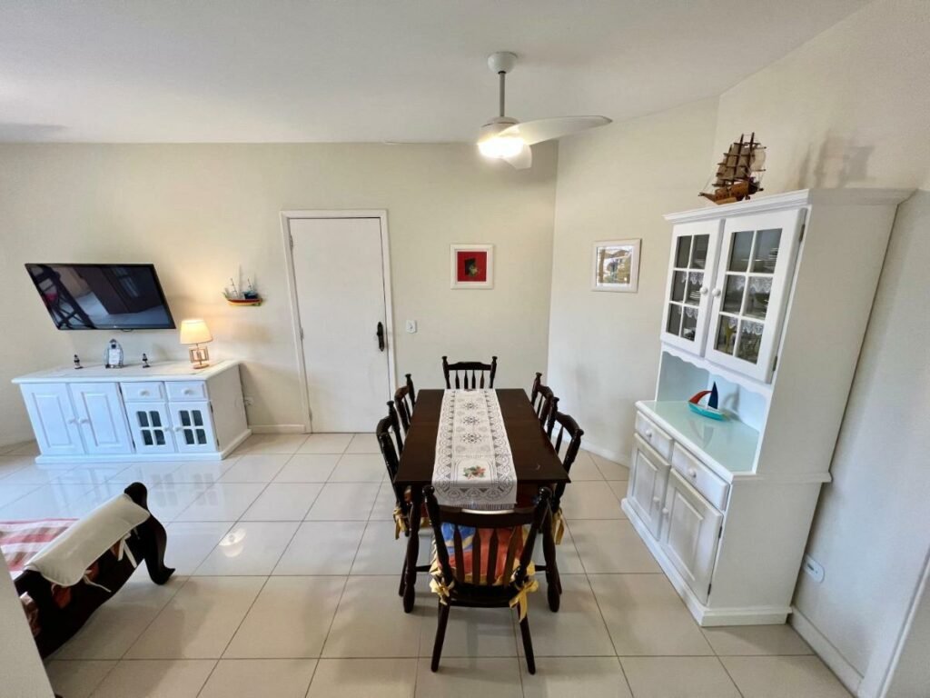Sala do airbnb Pontal das Marinas Frente Ilhabela. Do lado esquerdo está o sofá de frente para um móvel e a tv. Do lado direito há uma mesa de seis lugares e um armário com utensílios.