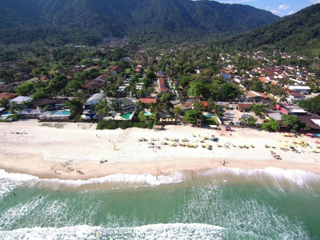 Vista aérea da praia de Maresias com mar em tom de verde, uma faixa de areia grande e tudo cercado por montanhas
