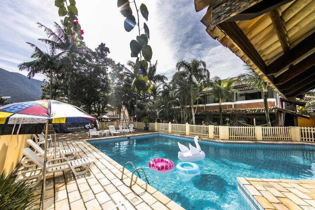 Piscina do Pousada Brig Maresias com um deck ao redor com espreguiçadeiras e guarda-sóis, além de algumas árvores