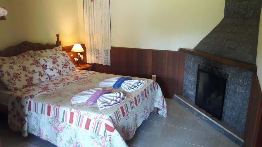 Quarto com cama de casal colorida, abajur ao lado e lareira.