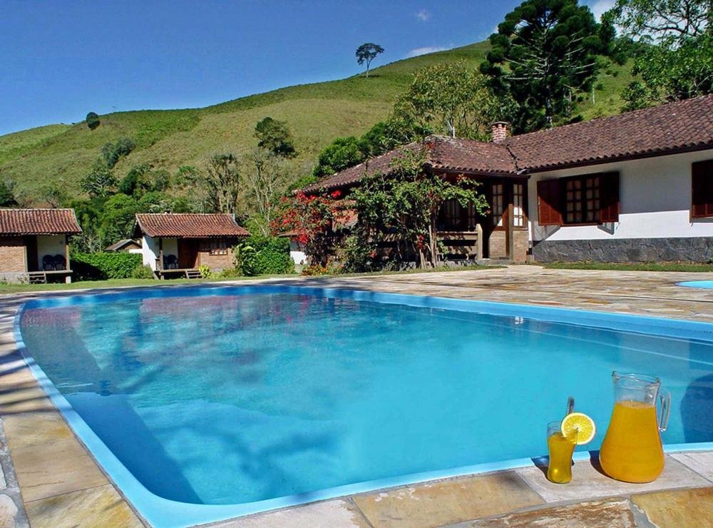 Piscina perto de casinhas brancas com flores e árvores em volta durante o dia, ilustrando post pousadas em Visconde de Mauá.