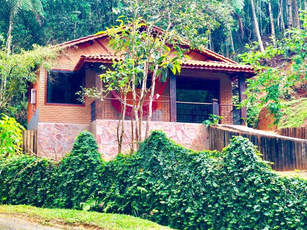 Casa de tijolos com rede vermelha na varanda e muitas árvores em volta durante o dia, ilustrando post pousadas em Visconde de Mauá.