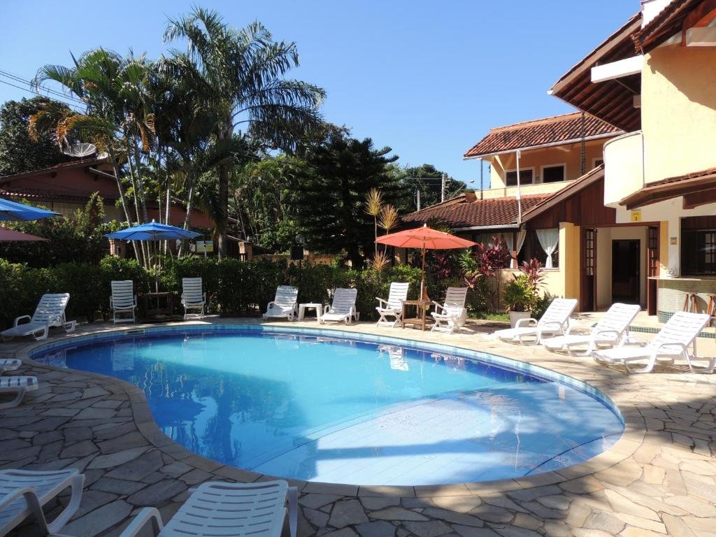 Piscina da Pousada Mosaico Brasil - Maresias com espreguiçadeiras brancas ao redor dela, para representar pousadas pé na areia em Maresias