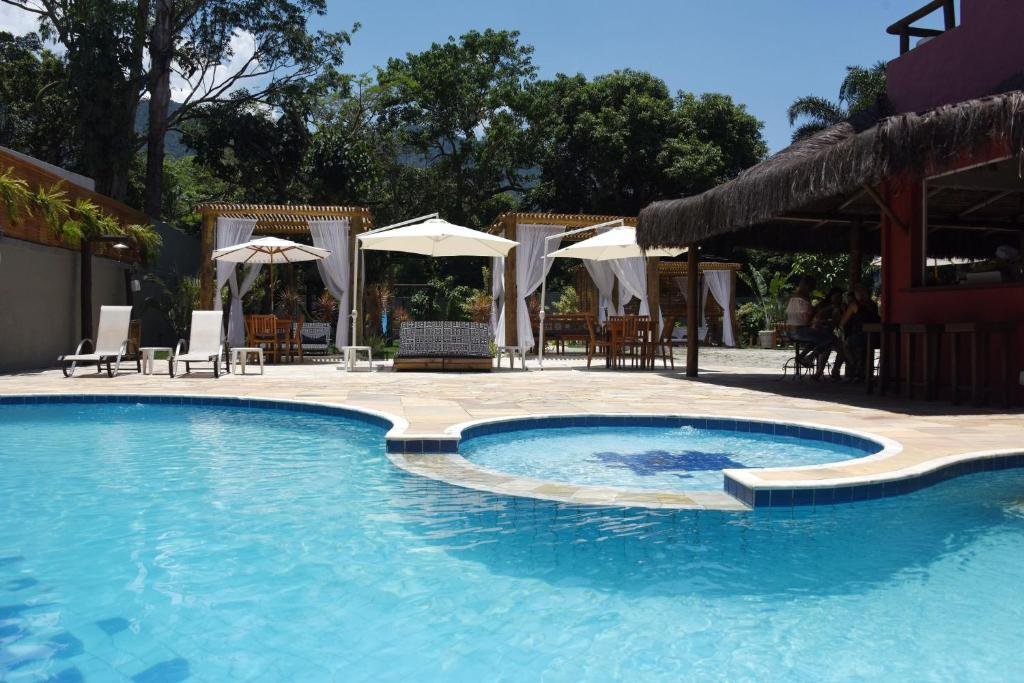 Piscina da Pousada Porto Mare com alguns bangalôs no deck com locais para se sentar com almofadas e espreguiçadeiras para pegar sol